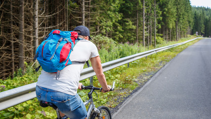 Fototapeta premium Young man with backpack cycling on road in mountains. Bicycle tourism background with copy space