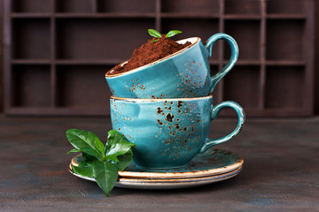 Still life with coffee cup, ground coffee beans and fresh leaves  on dark background
