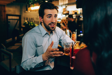 Handsome guy is talking to girl he likes. He is full in making conversation with her. Both of them have some drinks in their hands.