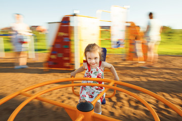 little girl spinning on a children's carousel among the playground.
