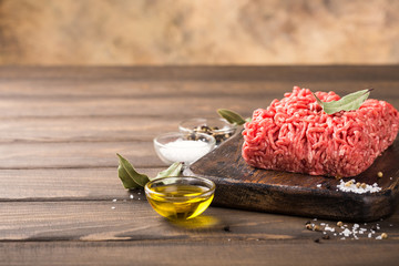 Fresh raw beef minced meat with salt, pepper, olive oil and laurel leaves on dark wooden board....