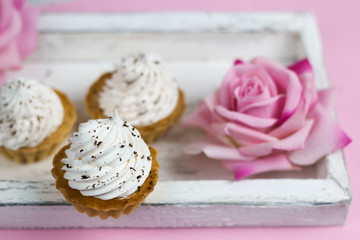 cute vanilla cupcakes on vintage wooden tray with rose flowers pink background