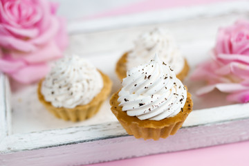 cute vanilla cupcakes on vintage wooden tray with rose flowers pink background