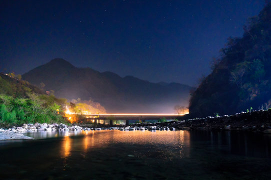Night shot of landscape with bridge over a still river and mountains in the distance and reflections in the water. Shot in Haridwar rishikesh india. perfect as a tourist travel shot