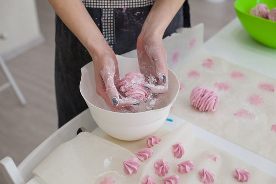 Woman's hands Sprinkling with Icing Sugar a Zephyr . Confectioner Sprinkles Powdered Sugar on pink crimson Marshmallow