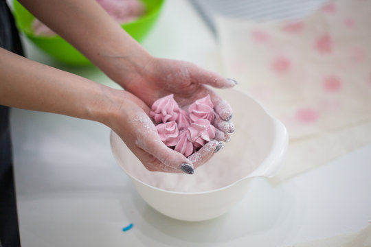 Woman's hands Sprinkling with Icing Sugar a Zephyr . Confectioner Sprinkles Powdered Sugar on pink crimson Marshmallow