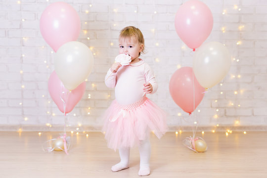 birthday party concept - little girl eating sweets over brick wall background with lights and balloons