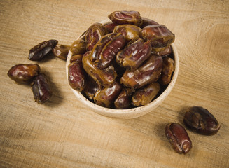 Dry dates fruit in the bowl, on the wood background.