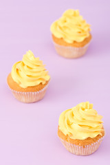 Cupcakes decorated with yellow cream on violet pastel background for greeting card with copyscape.