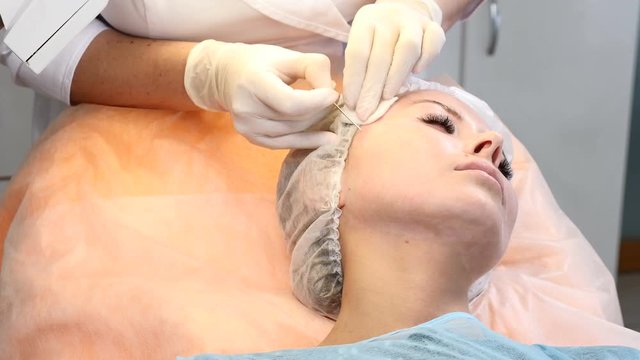 Beauty clinic. Young female client gets thread face lifting. Cosmetologist in gloves making face anti-aging to a female face