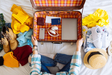 woman sit on bed with suitcase and clothes around. travel concept. decide warm or cold country to...
