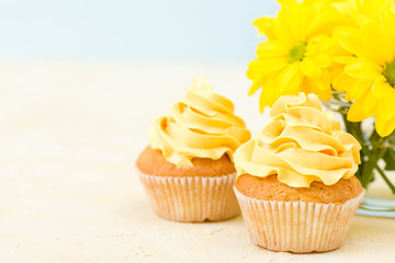 Cupcake with sweet yellow cream decoration and bouquet of yellow chrysanthemum in small glass