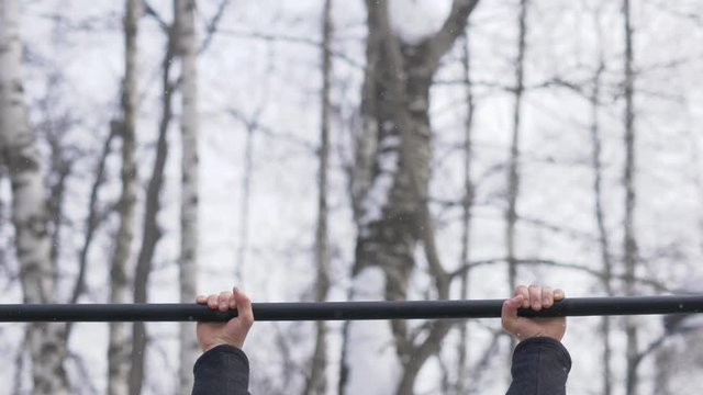 Young man doing pull up exercise on winter training on sport ground close up