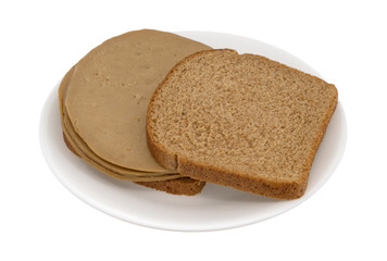 An opened face tofu turkey sandwich on wheat bread on a plate isolated on a white background.