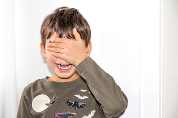 Junge steht vor weißer Wand und hält sich die Augen zu