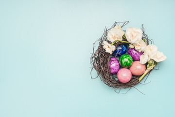 multi-colored easter eggs in a decorative nest with narcissus flowers, on a blue background, space for text
