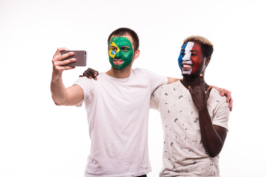Football fans supporters with painted face of national teams of France and Brazil take selfie isolated on white background
