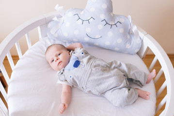 Beautiful newborn baby lying in an round bed with beautiful bumpers in delicate gray, blue, white tones