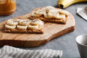 Two toasts from multi grain breads with peanut paste, banana slices and chia seeds on a serving wooden board. The concept of healthy fitness breakfast.