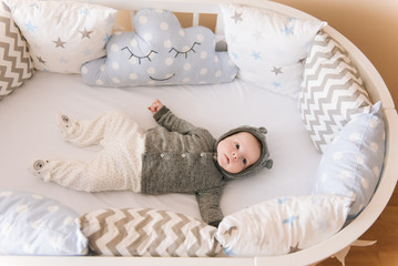 Beautiful newborn baby lying in an oval bed with beautiful bumpers in delicate gray, blue, white...