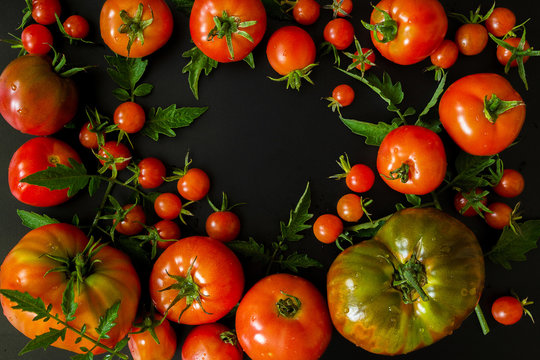 Set of a tomato of different varieties with leaves on a black background with copy space of a flat lay top view of a layout, a concept of a healthy diet, veganism