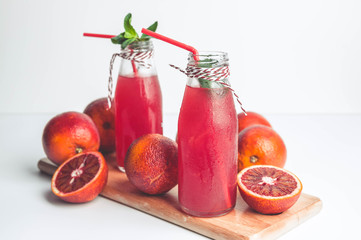 Blood oranges on a cutting board and juice in a glass bottle on a white background.