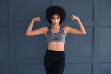 Fototapeta na wymiar Be active, be healthy, be happy! Beautiful young strong model in good shape posing for the camera isolated on the dark grey background and demonstrating her muscles.