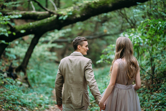 A happy couple is walking on a trail in an autumn forest. Bride and groom are looking at each other on nature.