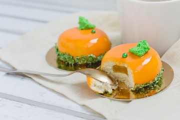 Bright orange mousse cakes and cup of coffee on white wooden tray