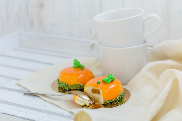 Bright orange mousse cakes and cup of coffee on white wooden tray