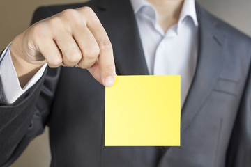 Business man in suit, holding in hand yellow Paper card for text. Copy space