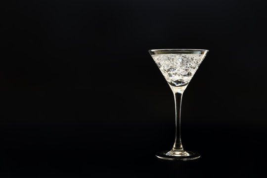 Cocktail with crystal like crushed ice in a martini glass outlined with back light against black background. Space for text