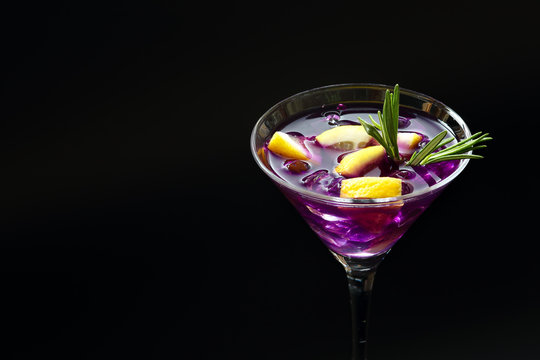 Fresh summer Purple rain cocktail in a martini glass with lemon slices on a black textured surface