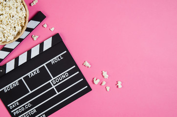 Fresh popcorn and movie clip isolated on pink background top view with copy space around products....
