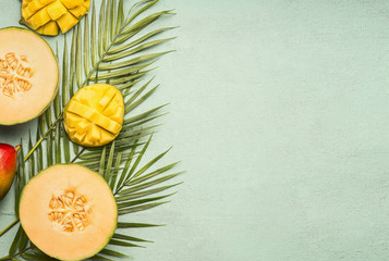 fresh cut melon and mango laid on tropical leaves on a blue rustic background, space for text, top view flat lay