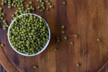 Organic mung beans on white ceramic bowl over wooden background.