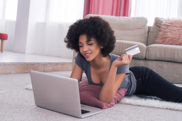 Let your online shopping be easy! A graceful beautiful young woman lying on the floor near her laptop and shopping with the credit card.