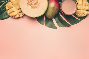 healthy food, tropical fruits, mango, melon on a monstera leaf with smoothies on a pink background, space for text flat lay