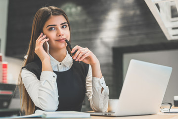 The attractive businesswoman phones near the modern laptop