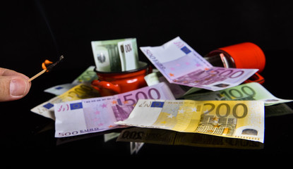 Burning euro banknotes with a matches. Reflection of euro banknotes on a black glass