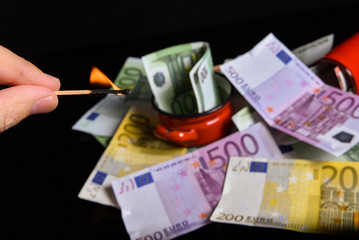 Burning euro banknotes with a matches. Reflection of euro banknotes on a black glass