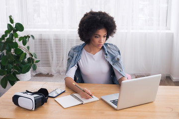 Make your work easy! Attractive African American lady writing and working on her laptop with a...