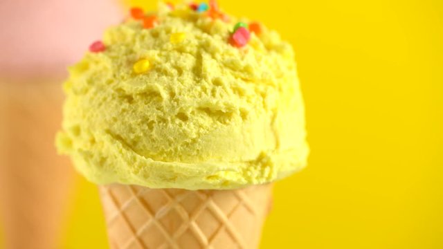 Ice cream. Vanilla, banana or lemon flavor icecream in waffle cone rotated over yellow background. Sweet dessert decorated with colorful sprinkles closeup. 4K UHD video footage. 3840X2160
