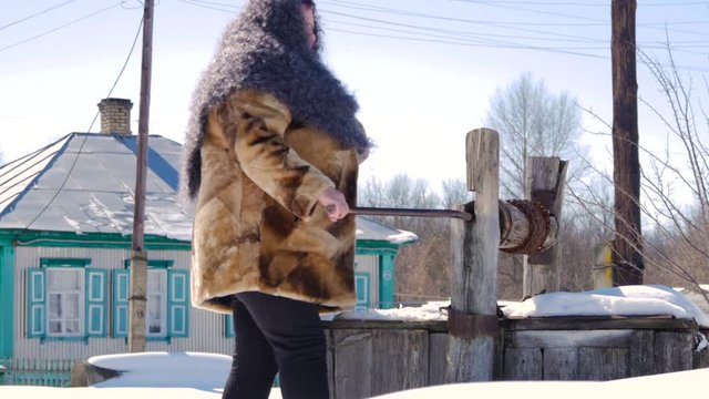 woman in winter clothes draws water in a wooden well
