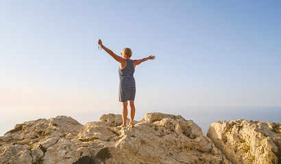 Happy middle-aged woman in blue dress greets the sun dawn and enjoying life summer concept