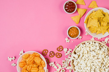 Fresh popcorn, snacks and chips in a bowl isolated on pink background top view. Frame composition with copy space. Movie watching concept