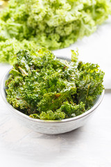 Kale chips in bowl. Crispy green kale chips dehydrated with salt, oil and vegan cheese. Healthy homemade vegan snack.