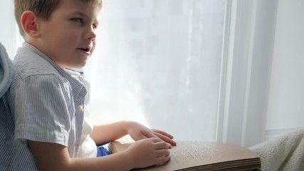 braille book in arms blind kid reading characters font sitting on windowsill indoors