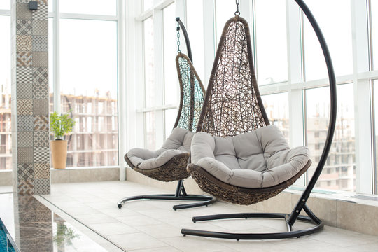 Modern comfortable hanging lounge chairs with soft pillows near panoramic window in recreation zone