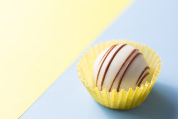 Homemade white chocolate truffle. One candy ball on yellow and blue table.